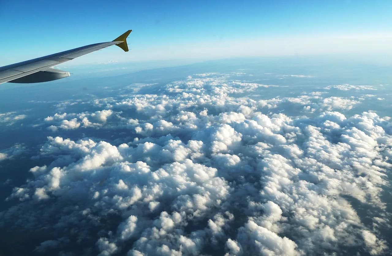 Krahu i një avioni fluturon mbi një det të gjerë reje nën një qiell blu të kthjellët.