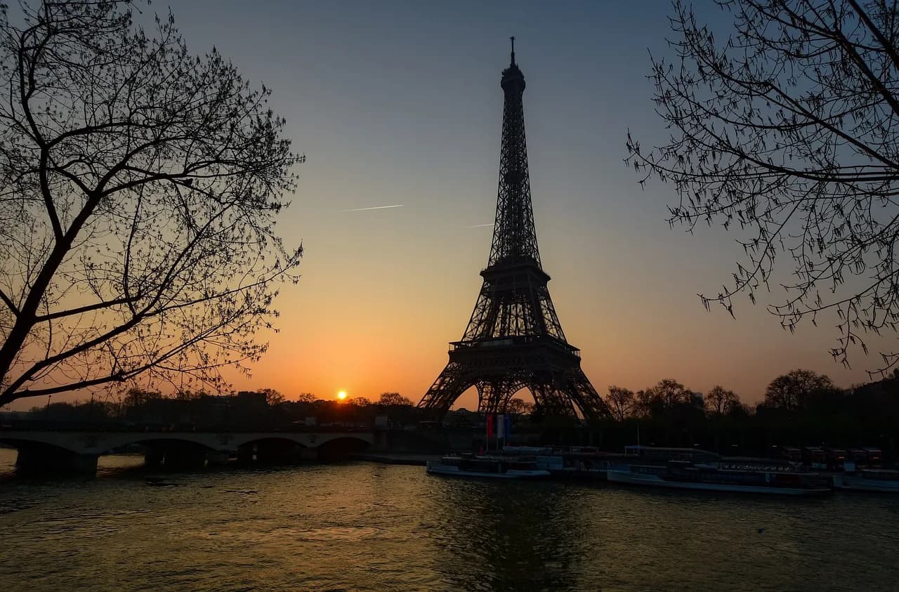 Kulla Eifel në lindje të diellit mbi Senë, Paris, Francë – siluetë e kornizuar nga pemet buzë lumit